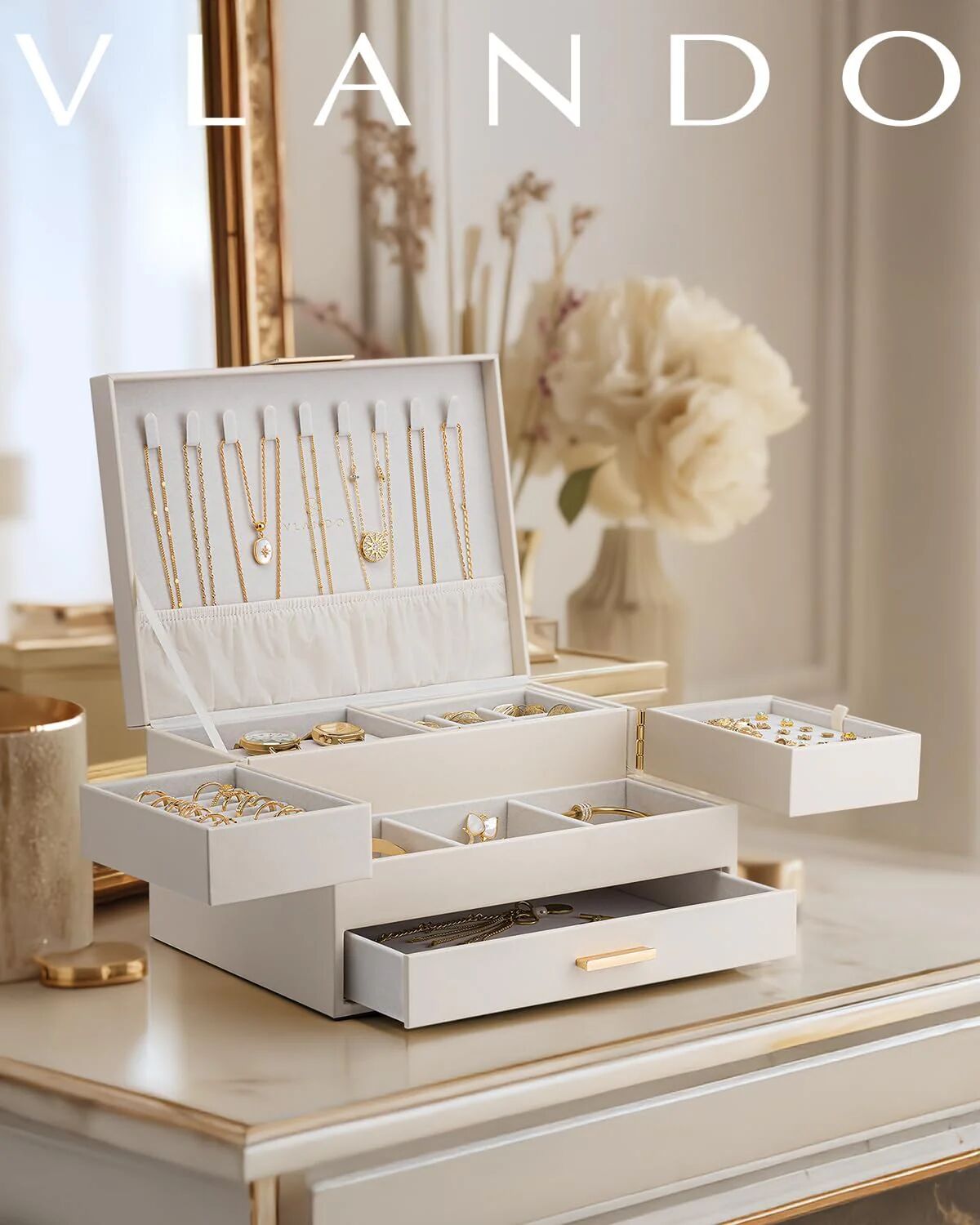 White multi-tiered jewelry box open on a marble vanity, displaying necklaces, watch, rings, earrings, and gold chains.